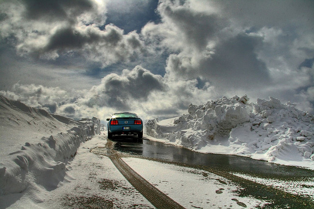 car driving up a hill in snow with clouds in the background