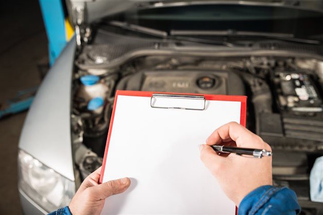 man holding clipboard in front of car with hood up