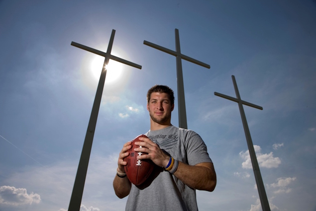 tim tebow holding football in front of three crosses