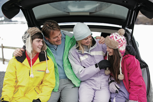 family sitting in back of suv in snow gear