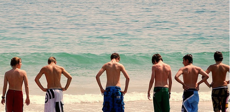 young guys wading in the water at beach, peeing