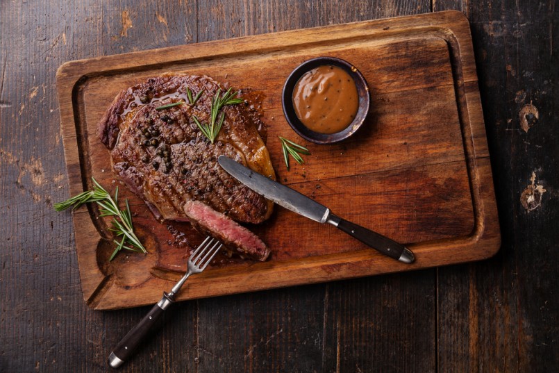 Grilled Black Angus Steak Ribeye and Pepper sauce on meat cutting board on dark wooden background