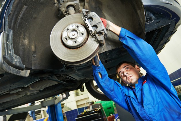 car mechanic examining car wheel brake disc and shoes of lifted automobile at repair service station