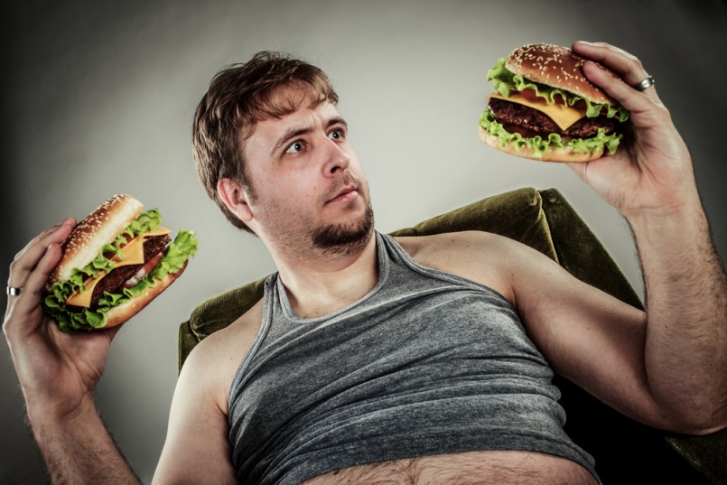 Fat man eating hamburger seated on armchair