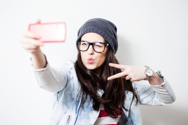 Pretty hipster girl taking selfie and making duck face. Sending kisses and holding peace sign. Instagram
