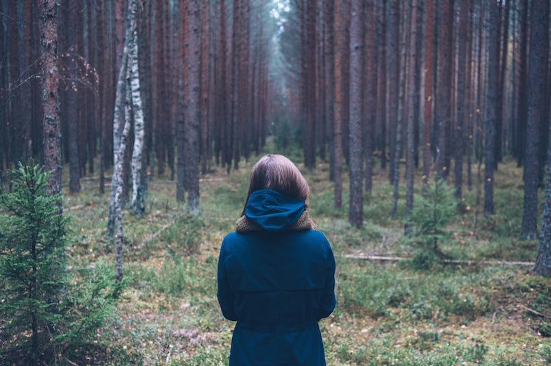 woman standing in forest looking at trees alone