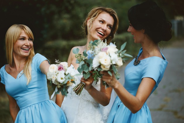 Stylish young smiling blonde bride with her bridesmaids in blue summer dress in the park on her happy wedding day