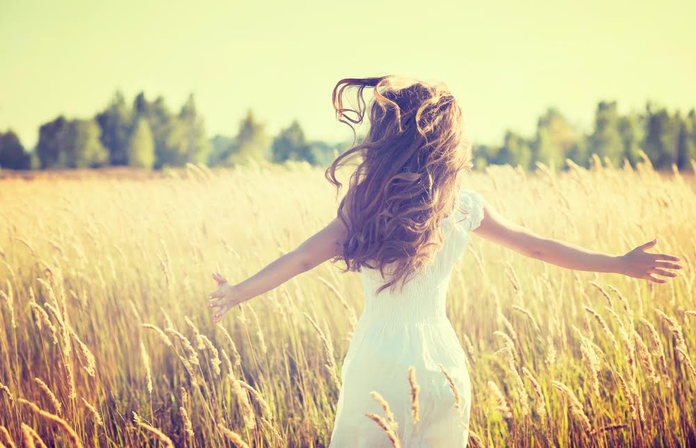 Beauty Girl Outdoors enjoying nature. Beautiful Teenage Model girl in white dress running on the Spring Field, Sun Light