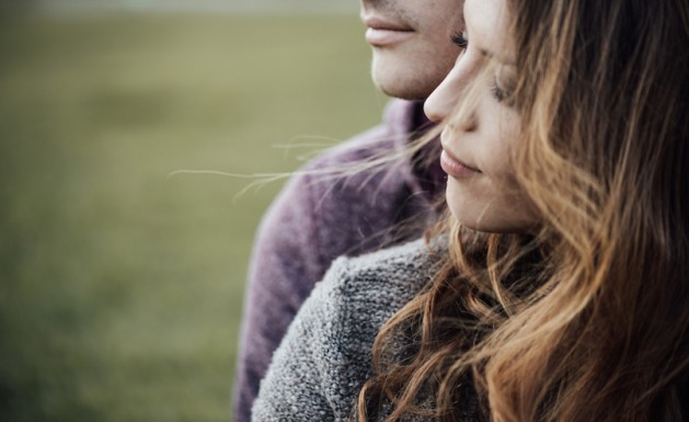 Young loving couple outdoors sitting on grass, hugging and looking away, future and relationships concept