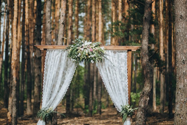 arch for the wedding ceremony, decorated with cloth flowers and greenery, is in a pine forest