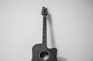 black and white photo of acoustic guitar leaning against a wall