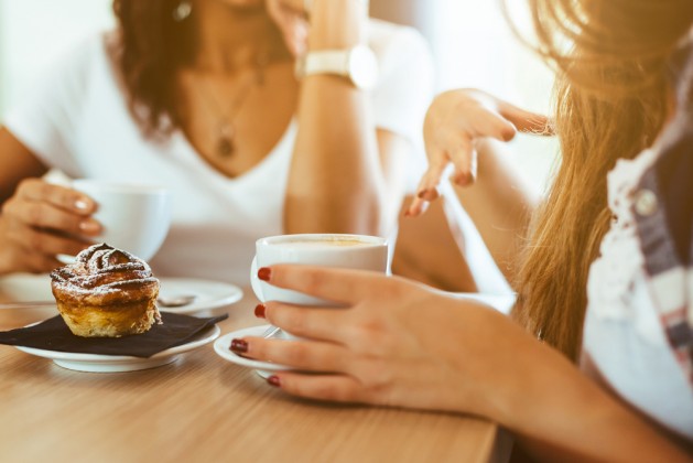 Two young and beautiful women meet at the bar for a cappuccino and to chat. A woman speaks gesturing while the other is listening