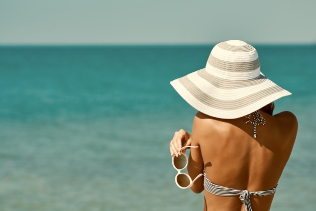 Sexy back of a beautiful woman in bikini, creative hat and sunglasses on sea background. Retro vintage toned image, film simulation.