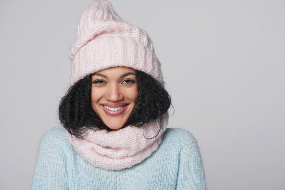 Laughing mixed race african american - caucasian girl wearing knitted sweater and hat with scarf, over gray background