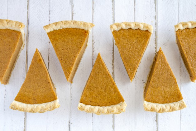 7 slices of homemade pumpkin pie in row sitting on white wooden table