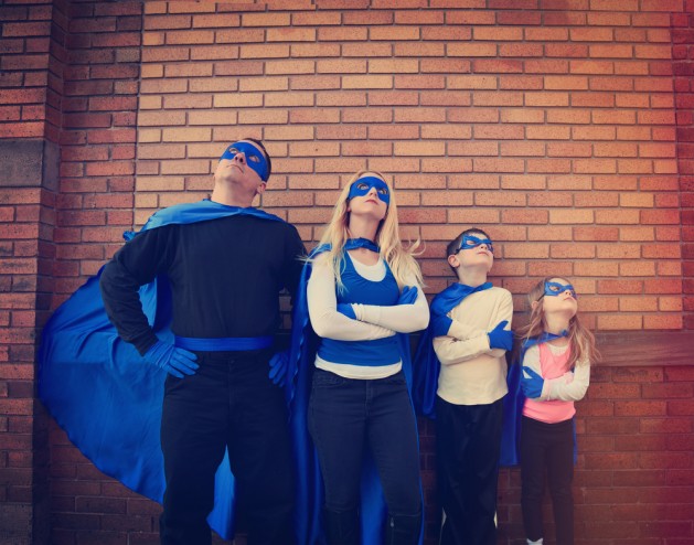 A young family of super heroes are standing outside with blue capes and masks looking up for a protection, strength or creativity concept