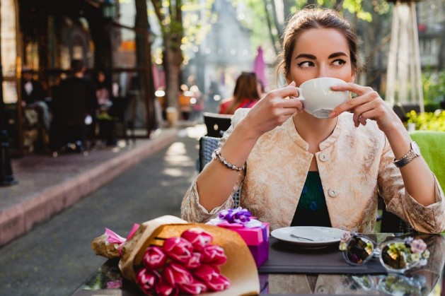 young stylish woman, fashion sunglasses, sitting in cafe, holding drinking cup cappuccino, enjoying, tulips, happy birthday party, city street, boho outfit, europe vacation, romantic dinner, sunny