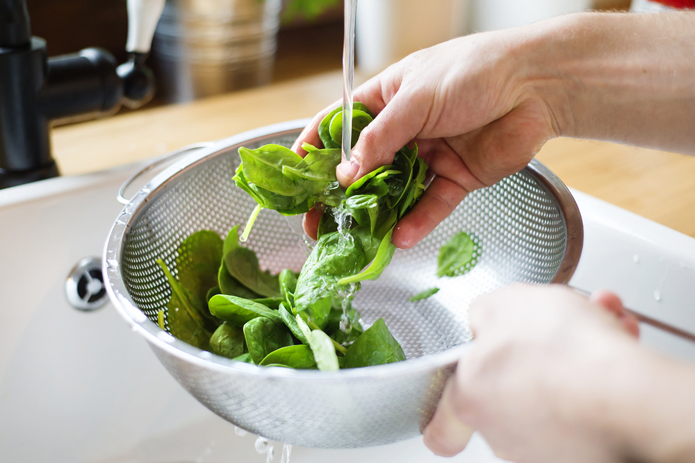 Unrecognizable man washing green salad leaves in the kitchen sink