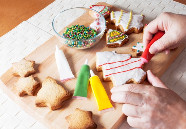 A detail of a woman's hand which is decorating Christmas cookie in shape of christmas tree with red ornaments