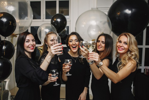 Cheers!Crazy party time of beautiful stylish women in elegant casual black outfit celebrating new year, birthday,having fun,dancing,drinking alcohol cocktails. Black and gold Balloons on Background women celebrating Galentine's Day