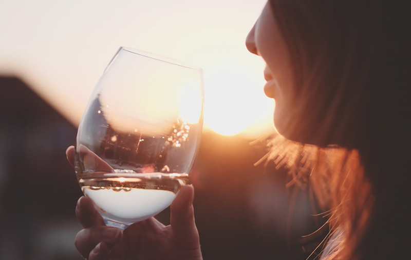 Woman Drinking Cooled White Wine from a glass at the Balcony during Sunset. Beautiful female enjoying cozy evening on terrace. Summertime relax at sunny patio. Lens Flare