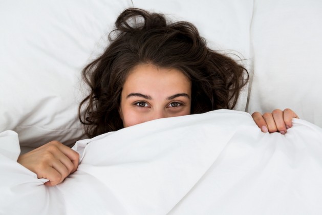 Woman hiding under blanket on bed at bedroom
