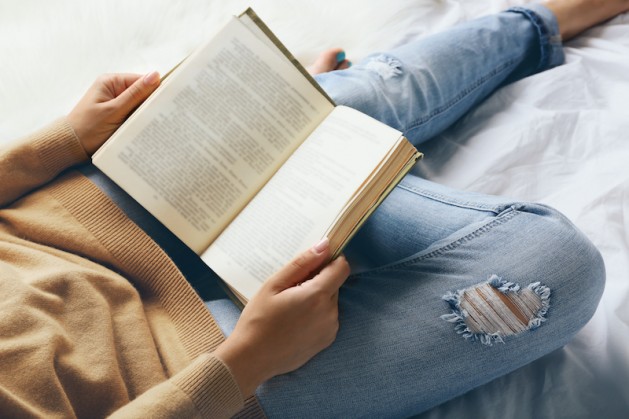 Woman in blue jeans reading book on bed top view point reading to sharpen brain 