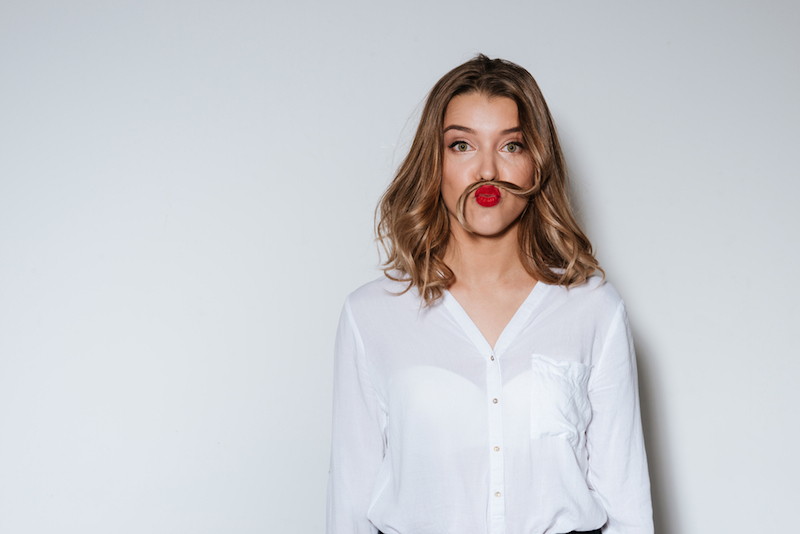Young funny woman making mustache with a long strand of her hair in a humorous way over white background boost your mood