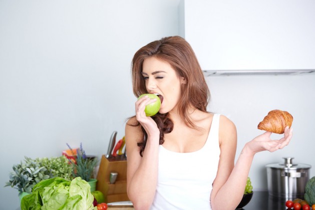 Diet. Dieting concept. Healthy Food. Beautiful Young Woman choosing between Fruits and Sweets