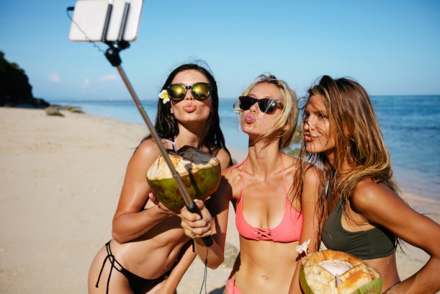 Three young women in swimsuit on the beach enjoying holidays and taking self portrait selfie stick. Group of female friends with coconuts taking selfie on the sea shore. Pout for a selfie on beach, how to eat for a healthy gut