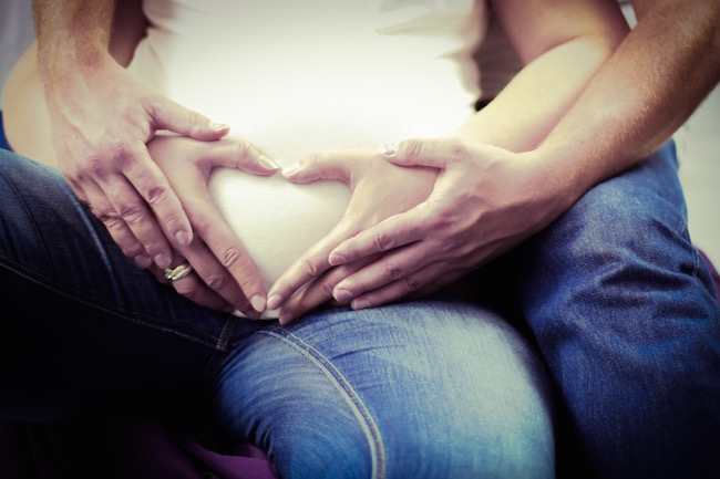 man holding pregnant woman's stomach with her hands forming a heart