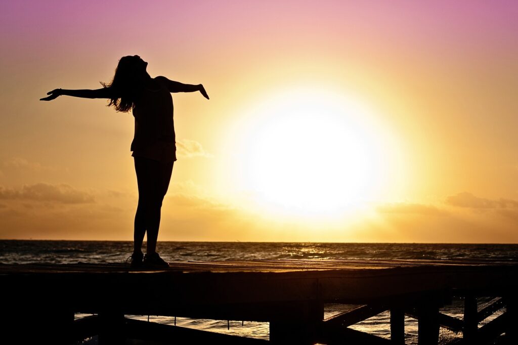 Woman looking up at the sky with arms open and sunset in background